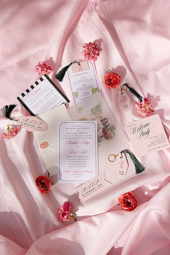 Invitation suite wedding invitation flat lay with wax-sealed envelopes, RSVP and menu cards, coral ranunculus on a pink satin backdrop
