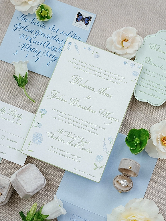 Wedding invitation suite with letterpress wedding invitation, calligraphy envelope and RSVP card beside a vellum ring box and flowers on linen background