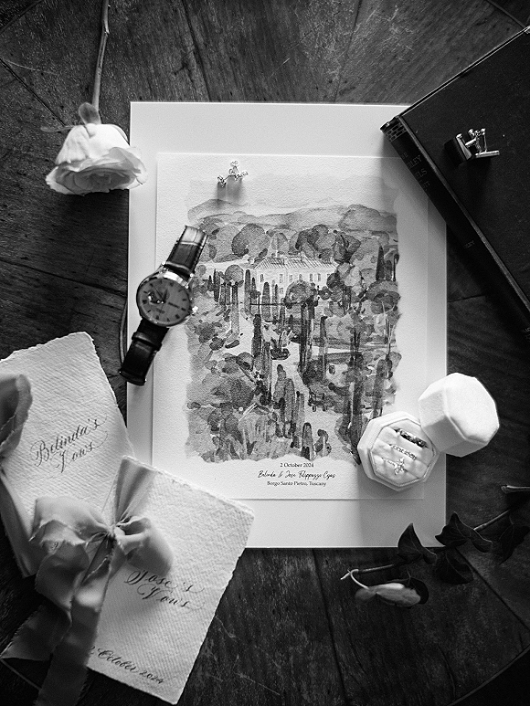 Invitation suite wedding invitation flat lay on a wood tabletop with watercolor card, silk ribbon, wax seal, rings, watch, and rose accent