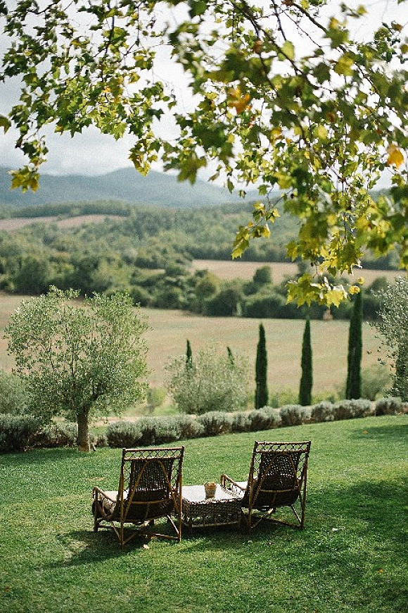Outdoor lounge seating with wicker chairs and a low coffee table, decorative pillows and glassware set on a lawn with mountain views