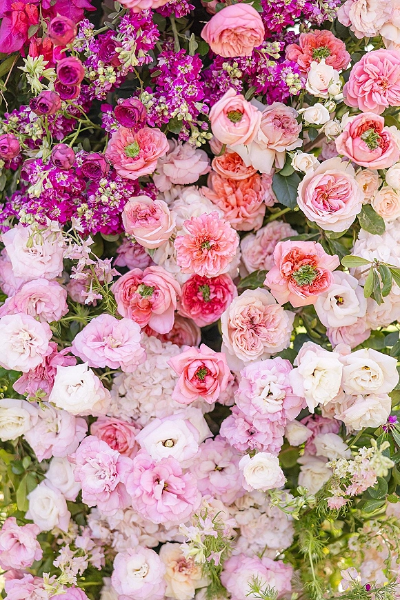 Wedding floral wall with layered roses and ranunculus blooms and greenery, forming a dense pink-to-fuchsia flower wall backdrop