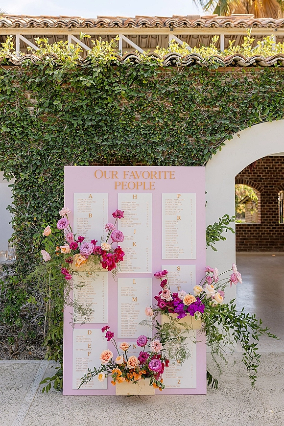 Seating chart wedding seating chart board in pink with white cards, roses and greenery accents, plus glass votive candles against an ivy wall