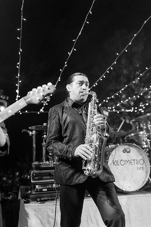 Wedding band playing live wedding music on an outdoor stage, with a saxophone player under string lights against trees and night sky