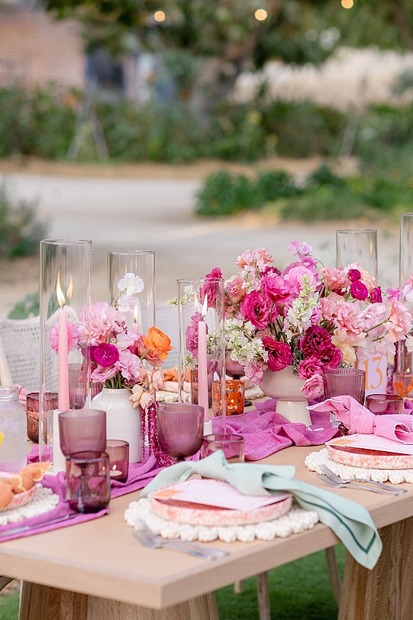 Reception tablescape with pink wedding tablescape florals, taper candles in glass hurricanes, colored goblets, and string lights in garden greenery
