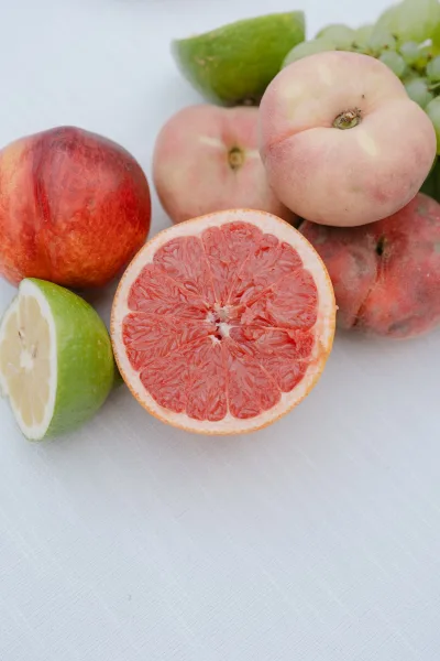 Wedding fruit styling with a grapefruit half surrounded by limes, peaches, and grapes arranged on a white linen tablecloth