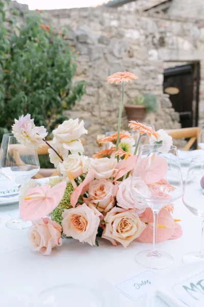 Reception centerpiece with wedding floral centerpiece of peach roses, anthurium and greenery on a white table, stone wall behind
