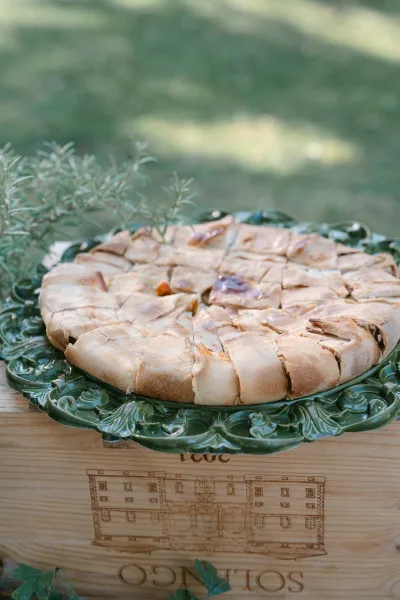 Wedding dessert display on a green ceramic platter with rosemary sprigs on a wooden crate, set on an outdoor lawn with greenery backdrop