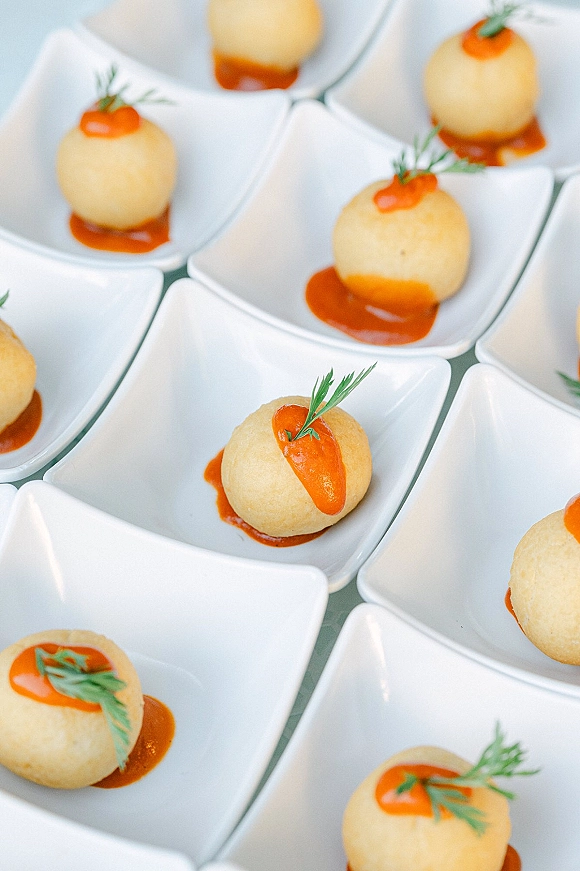 Wedding appetizers in white porcelain bowls with bite-sized hors d'oeuvres topped with red sauce dots and herb garnish on a catering display surface