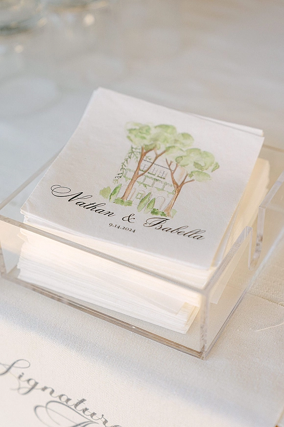 Wedding napkins and custom wedding napkins with calligraphy names and watercolor illustration in an acrylic holder on a white tablecloth