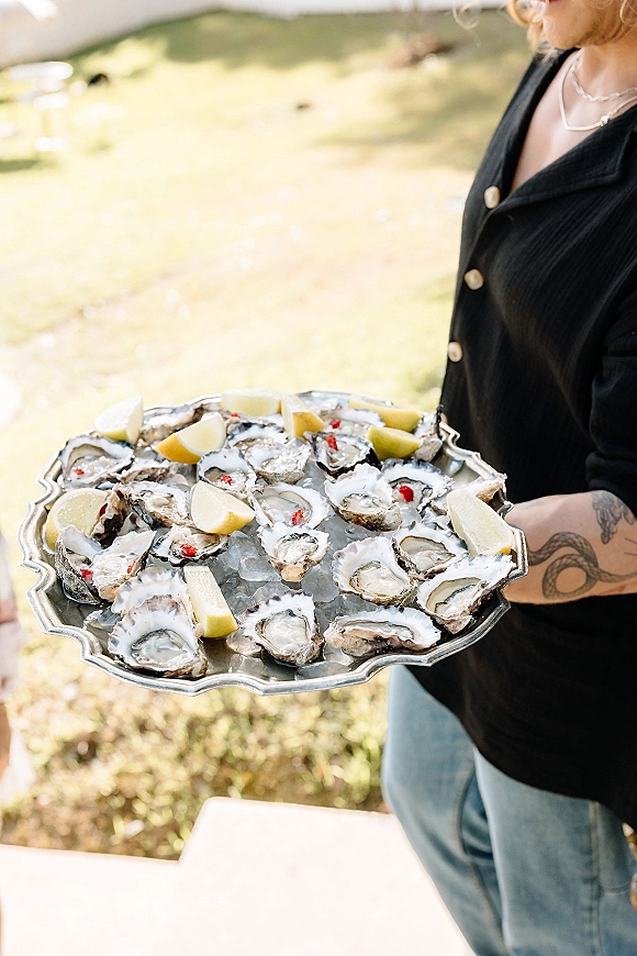 Oyster platter at a wedding oyster bar on a silver tray with oysters on crushed ice and lemon wedges, set on a sunlit lawn