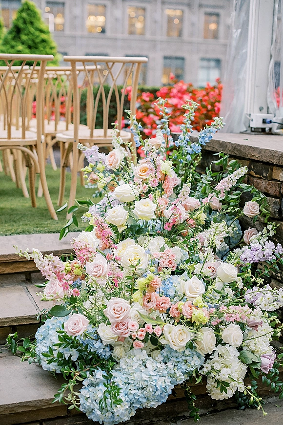 Wedding ceremony flowers with roses and hydrangea in a ground floral arrangement lining stone steps, with chiavari chairs in a courtyard lawn