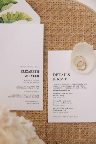 Wedding invitation suite with tropical invitation design, accented by gold rings, styled on woven rattan.