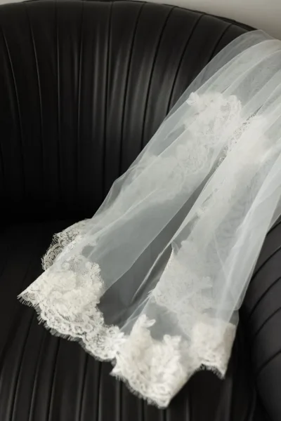 Bridal veil, a lace wedding veil with delicate lace trim, draped over a black leather chair, highlighting its delicate edge detail.