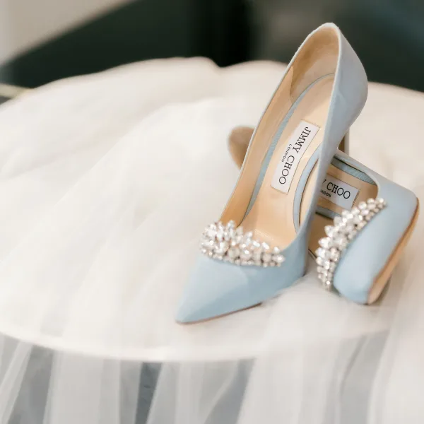 Bridal shoes in blue wedding heels with crystal embellishments, styled beside a tulle veil on a soft fabric surface indoors
