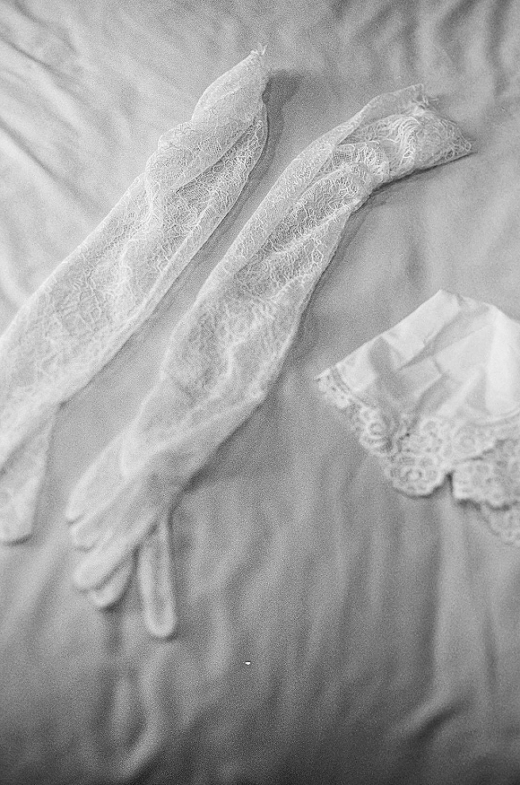Bridal gloves with lace wedding gloves detail arranged beside lace lingerie on a bed sheet, showcasing delicate fabric folds and texture
