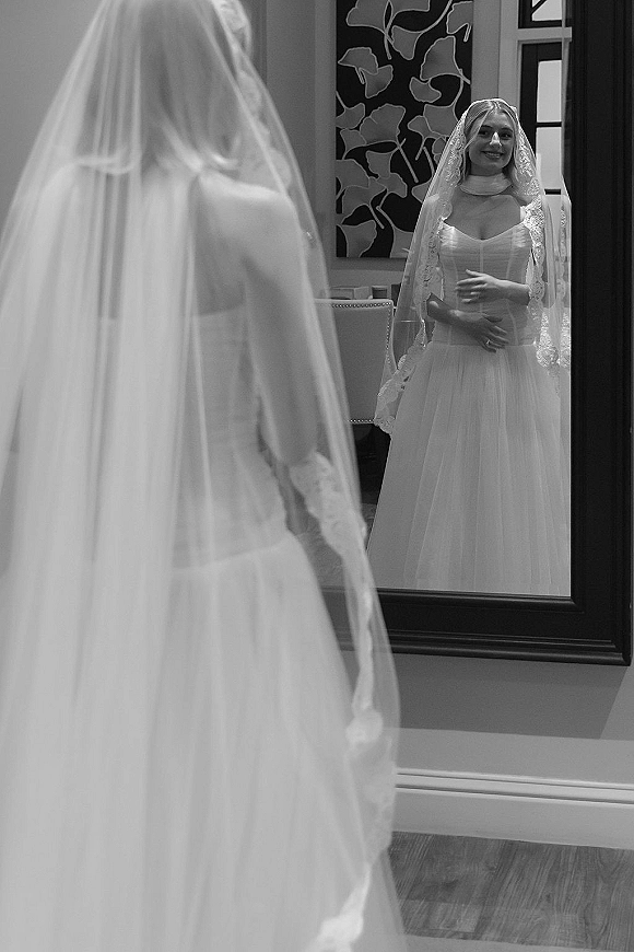 Bridal portrait of a bride in mirror wearing a strapless wedding dress and lace veil in an elegant room with wall molding and artwork