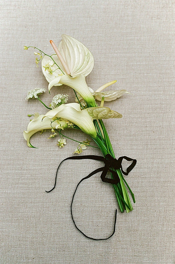 Bridal bouquet with calla lily bouquet featuring white calla lilies and anthurium, greenery, and black ribbon on linen backdrop