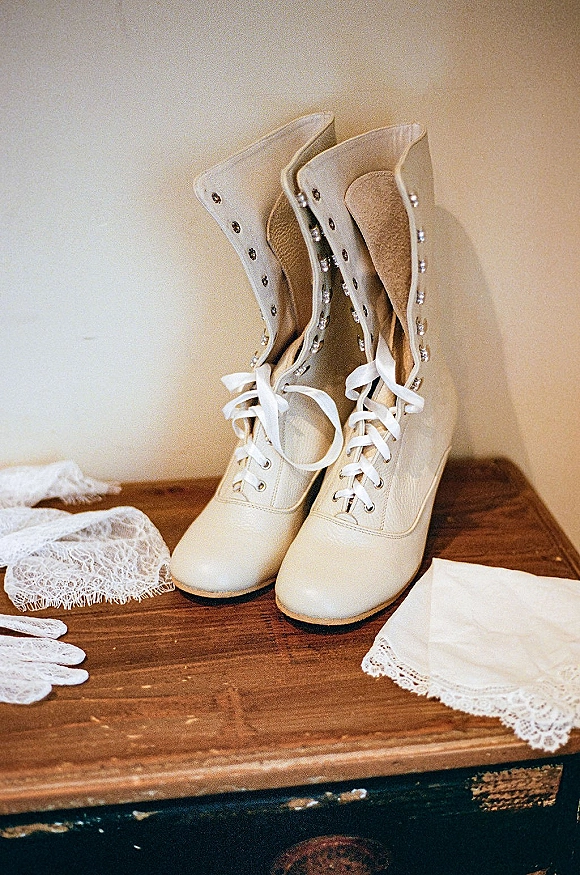 Bridal shoes—ivory wedding shoes lace-up boots with satin ribbon laces and rhinestone details on a wooden tabletop beside lace gloves