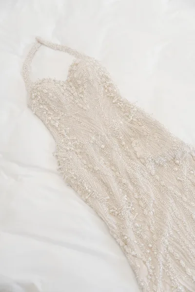 Wedding dress close-up of a pearl beaded wedding dress draped on white bedding, highlighting delicate textures and soft shimmer.