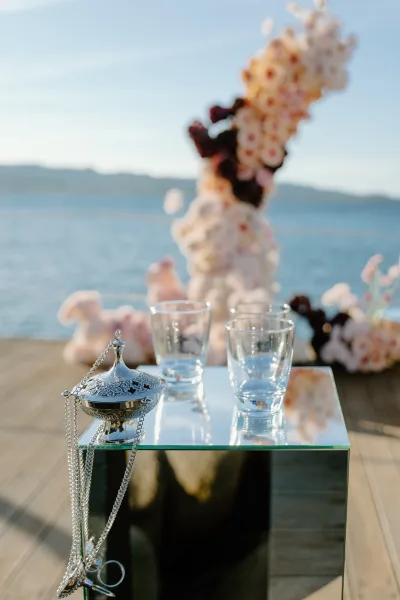 Ceremony table decor with modern altar detail featuring a mirrored pedestal on a wooden deck beside water, with mountains under an open sky.