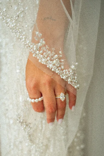 Engagement ring close-up featuring a marquise diamond ring in yellow gold, stacked with a wedding band atop a beaded wedding dress.