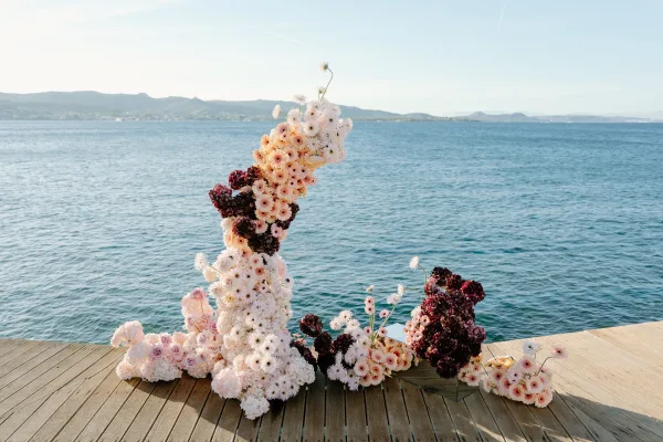 Ceremony floral installation forming a ground floral arch on a wooden deck, framing the ocean and distant hills beneath open sky.
