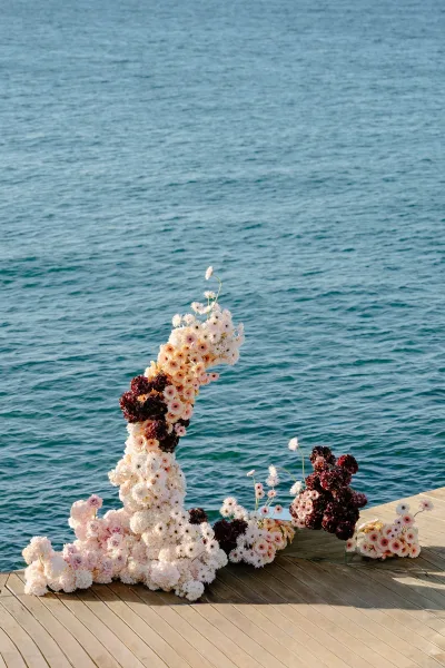 Floral ceremony backdrop creating a modern wedding altar, blooms styled on a mirror plinth on a wooden deck overlooking the ocean.