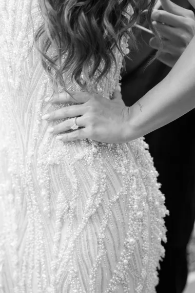 Engagement ring close-up on a bride’s hand with ring, fingers gently resting on a beaded wedding dress, highlighting the intricate beadwork.