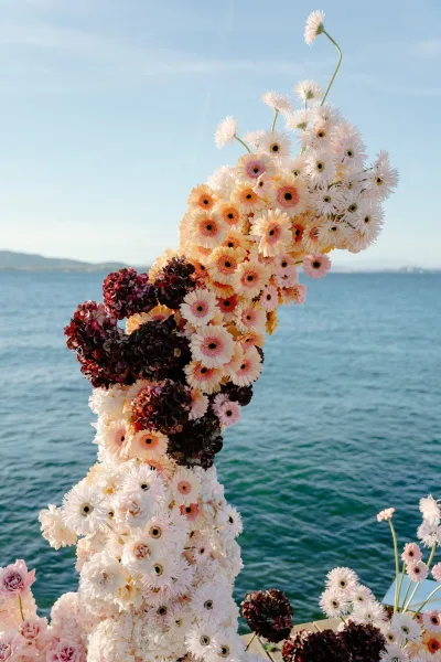 Ceremony floral installation of coastal ceremony flowers, featuring gerbera daisies, set against ocean water and blue sky with distant shoreline.