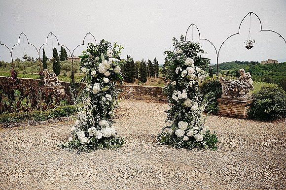 Wedding ceremony backdrop with outdoor wedding altar flowers, lush white hydrangeas and greenery around metal frames in a gravel courtyard