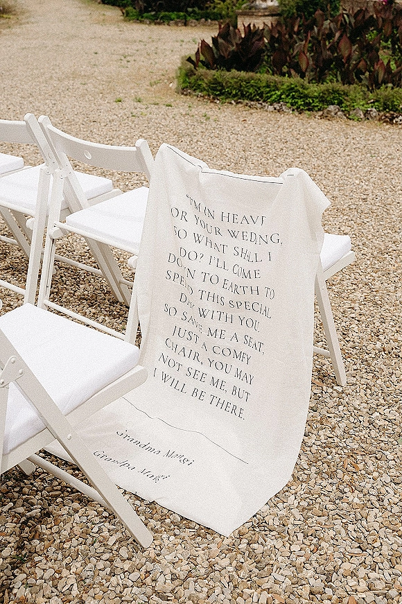 Wedding memorial seat with reserved seat wedding sign draped in fabric over a white folding chair beside a gravel aisle and garden plants