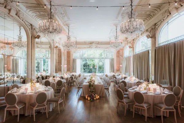 Wedding reception decor with elegant ballroom reception tables, white linens, floral garlands, candles, and crystal chandeliers in an ornate room