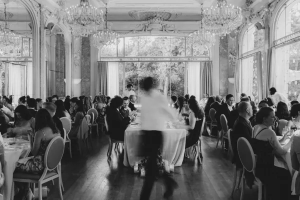 Wedding reception set with round tables, candlelit place settings, low floral centerpieces, and crystal chandeliers in a mirrored ballroom with large windows