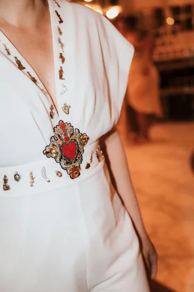 Bridal gown detail with wedding dress embroidery, showing a red heart patch with gold beadwork on the bodice against warm bokeh lights indoors