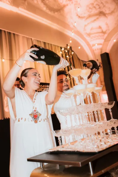 Champagne tower pour at a wedding champagne tower as sparkling wine cascades down coupe glasses under warm string lights and draped curtains