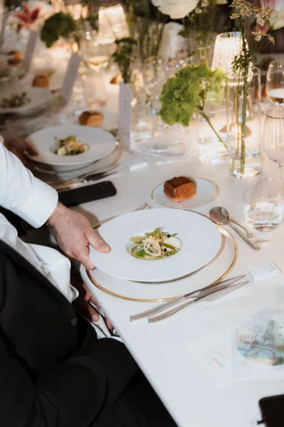Reception tablescape with wedding table setting featuring white linens, gold rim chargers, green hydrangea centerpieces, and candles on a long banquet table