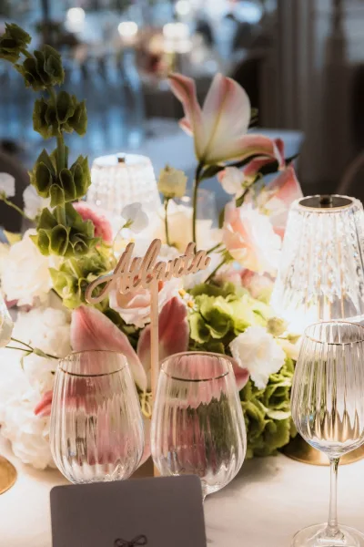 Reception tablescape with wedding table centerpiece of pink lilies, candles in ribbed glass votives, and calligraphy table number in ambient room lighting