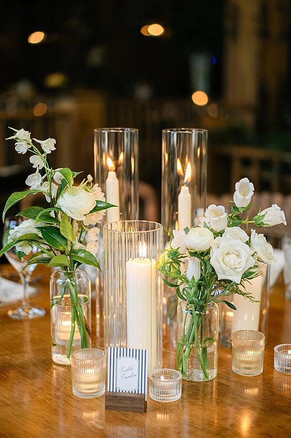 Wedding centerpieces with candlelit wedding centerpiece styling, white flowers and greenery in glass vases with taper candles under warm bistro lights