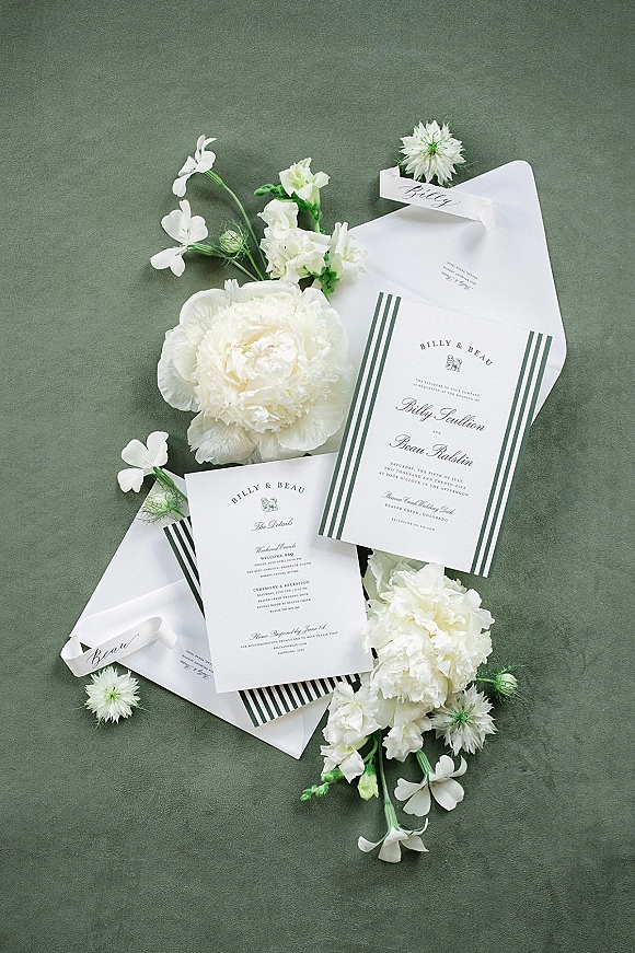 Wedding invitation suite with classic wedding invitations, envelopes and striped liner, tied with green ribbon on green fabric with white flowers