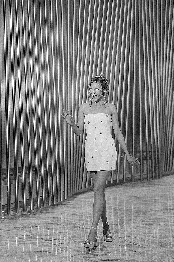 Bridal mini dress in a strapless, crystal-embellished white style with high heel sandals and an updo, posed before draped curtains