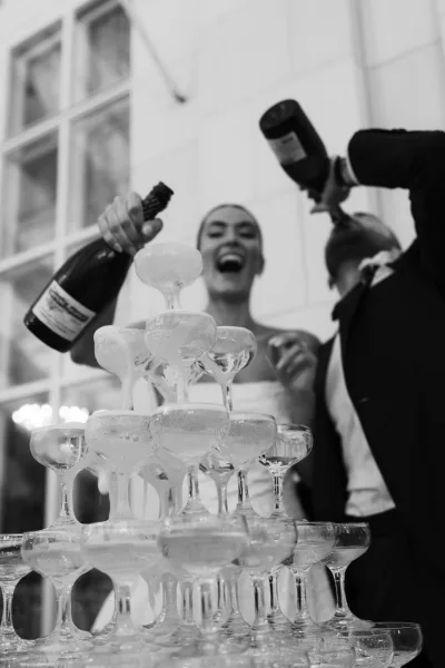 Champagne tower gleams during a wedding champagne pour, tiers of sparkling wine reflecting near a bride in a strapless gown.