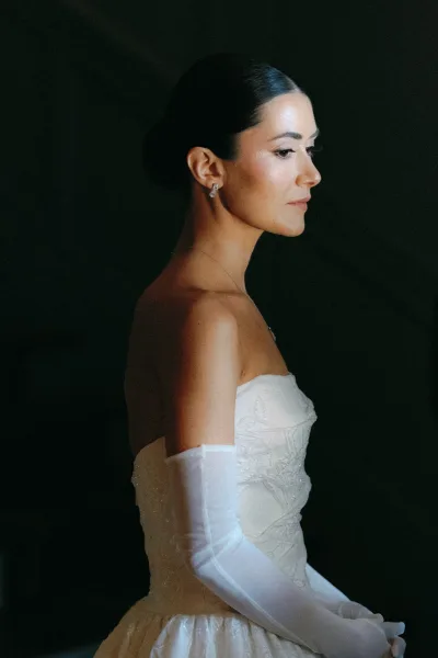 Bridal portrait of a bride in side profile wearing a strapless wedding dress with opera gloves, sleek low bun, and classic makeup for an elegant look.
