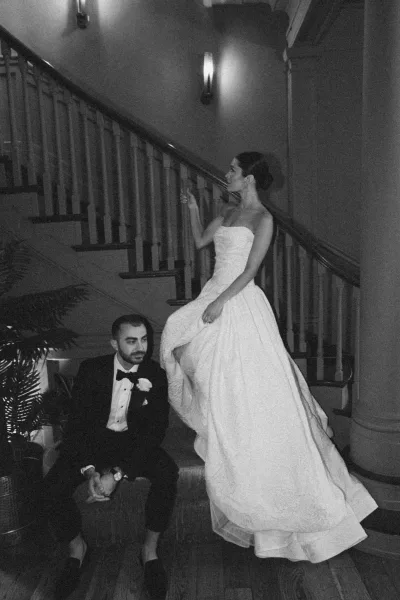 Couple portrait, a staircase wedding portrait with the bride toasting with a champagne glass beside her groom beneath warm wall sconces.