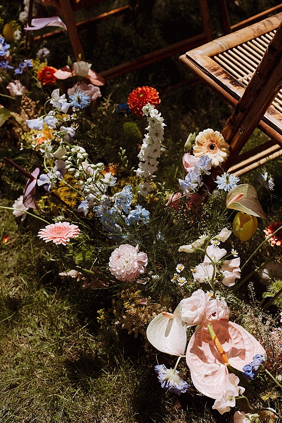 Ceremony aisle flowers in a ground floral aisle meadow of wildflowers with pink anthurium, daisies and bamboo chairs on a sunny lawn