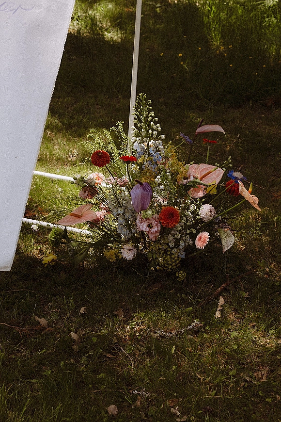 Wedding ceremony florals in a ground floral arrangement with anthurium, tulips, wildflowers, and draped fabric on a sunlit lawn