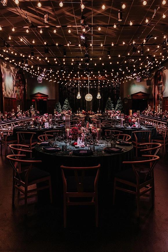Reception tablescape with candlelit wedding reception glow, velvet linens, floral centerpieces, taper candles, and string lights in a moody hall