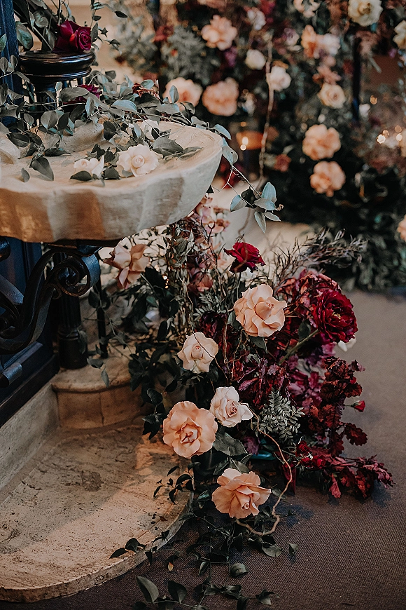 Wedding floral decor with a ceremony floral installation of rose arrangements and greenery garland on pedestal stands beside pillar candles indoors