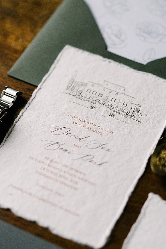 Wedding invitation suite with deckled edge wedding invitations, calligraphy details, wax seal and venue illustration arranged on a wood table