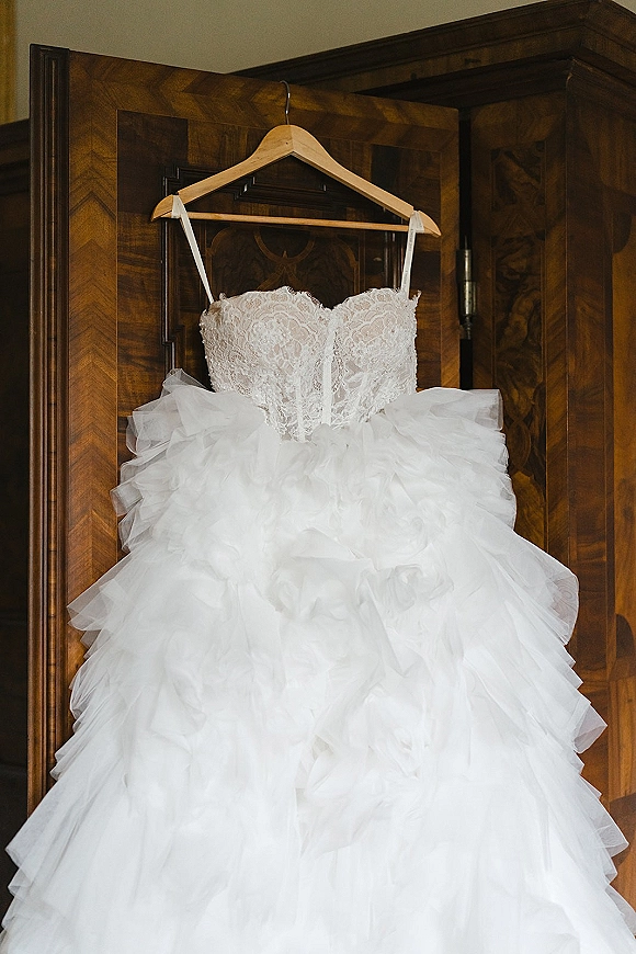 Wedding dress with lace bodice and voluminous tulle skirt on a wooden hanger, hanging inside a wooden wardrobe with doors open