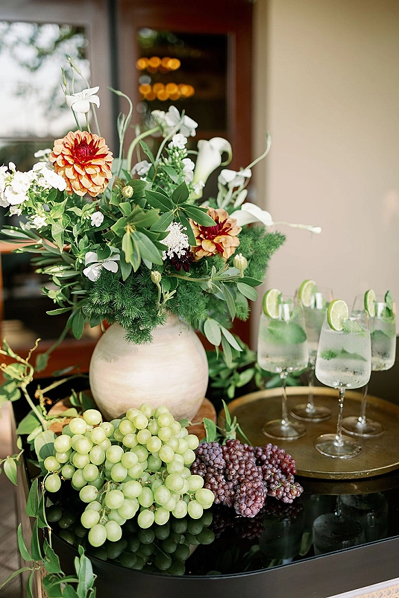 Wedding cocktail bar with wedding signature drinks, garnished glasses with lime and mint beside a floral centerpiece in a ceramic vase under warm bistro lights